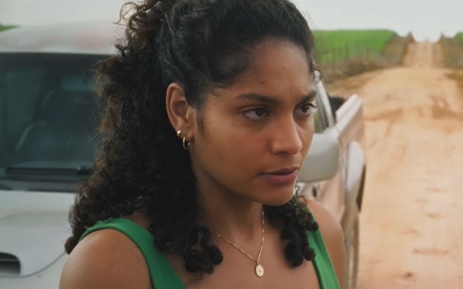 Barbara Reis caracterizada como Aline; ela usa uma camiseta verde e tem o semblante abalado em cena de Terra e Paixão