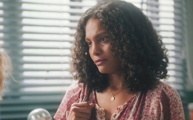 A atriz Barbara Reis está caracterizada como Aline em cena da novela Terra e Paixão: usa cabelos soltos e blusa estampada