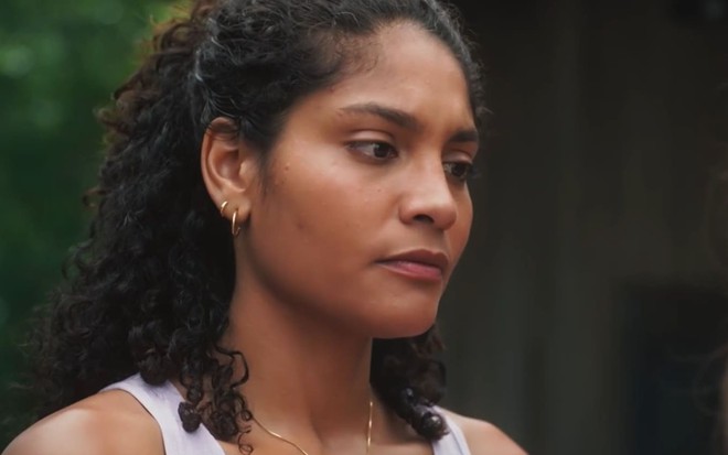 Barbara Reis caracterizada como Aline; ela usa uma camiseta vinho e tem o semblante abatido em cena de Terra e Paixão