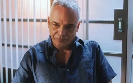 O ator Ângelo Antônio está sentado e faz uma expressão de desgosto em cena da novela Terra e Paixão como Andrade