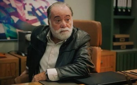 O ator Tony Ramos está sentado e usa casaco escuro e camisa clara em cena da novela Terra e Paixão como Antônio
