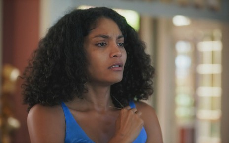 Barbara Reis interpreta Aline na novela Terra e Paixão com blusa regata azul e cara de sofrida