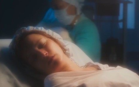 A atriz Bianca Bin como Agatha deitada desfalecida em um leito de hospital após dar à luz