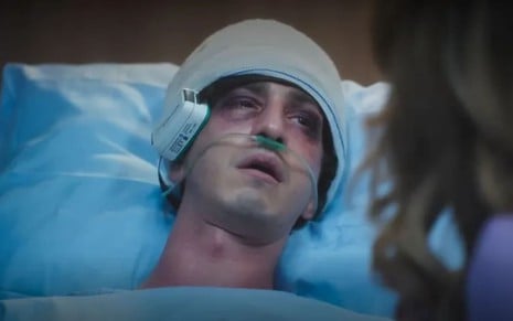 Johnny Massaro caracterizado como Daniel; ele está deitado num leito de hospital, com a cabeça enfaixada e os olhos roxos, em cena de Terra e Paixão