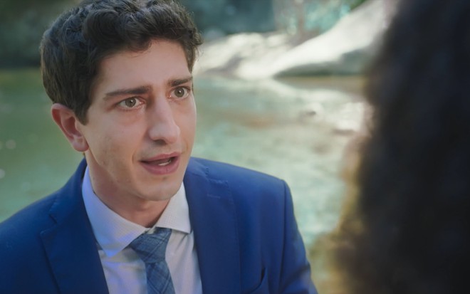 Johnny Massaro está de terno e gravata e com a boca semiaberta como Daniel da novela Terra e Paixão