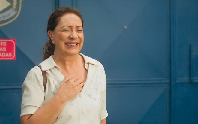 Em cena de Terra e Paixão, Eliane Giardini está emocionada, saindo do presídio; no fundo há um portão azul