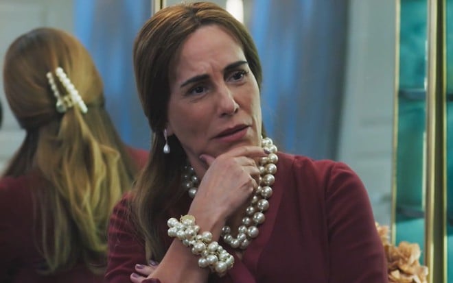 Gloria Pires caracterizada como Irene; ela está com os cabelos castanhos soltos, traja um vestido vermelho e usa joias exageradas de pérolas. O semblante exprime indignação em cena de Terra e Paixão