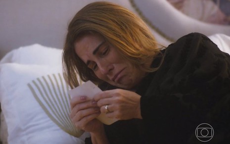 A atriz Gloria Pires usa roupa preta e está deitada olhando uma foto em cena como Irene na novela Terra e Paixão