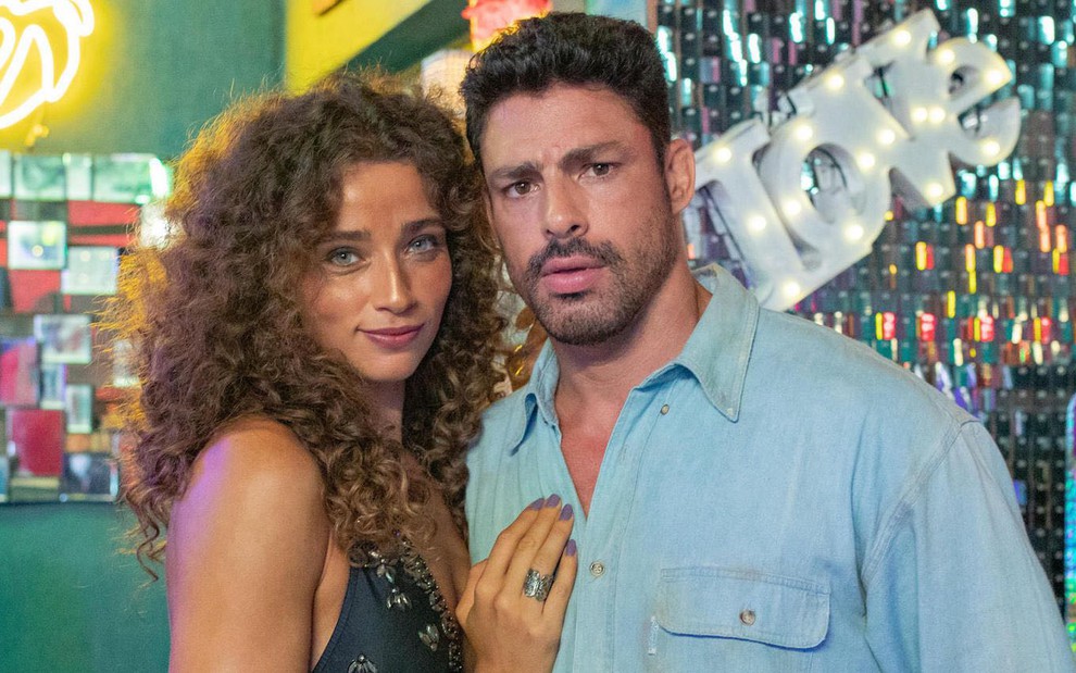 Letícia Laranja posa no cenário do bar de Terra e Paixão com Cauã Reymond; ela está caracterizada como Flor, e ele como Caio