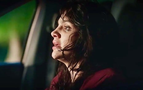 Debora Ozório está com maquiagem borrada e cabelo despenteado dentro de um carro como Petra na novela Terra e Paixão