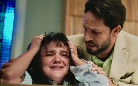 A atriz Debora Ozório está chorando agoniada em cena de Terra e Paixão na qual Rainer Cadete ampara a sua personagem, Petra