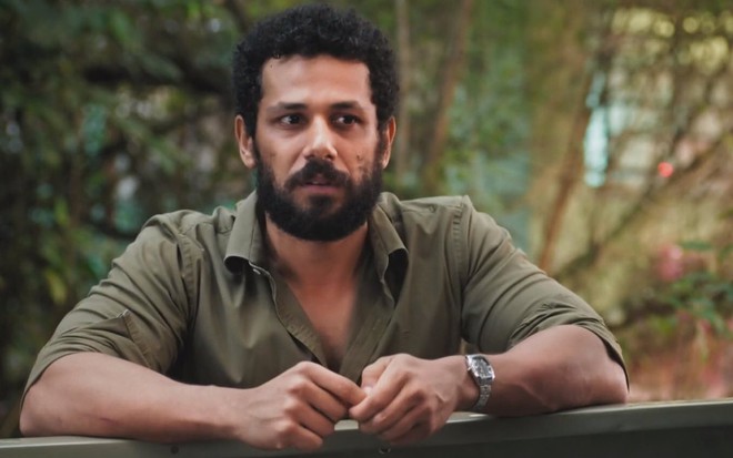 O ator Amaury Lourenzo está sério e usa camisa verde em cena de Terra e Paixão como Ramiro