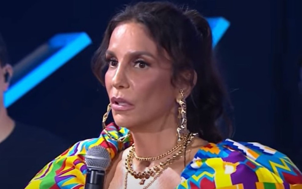 Com roupa colorida, Ivete Sangalo segura microfone enquanto fala no palco no Música Boa