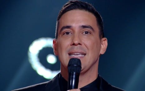 Andre Marques segura o microfone enquanto apresenta o The Voice Brasil; ele está todo de preto