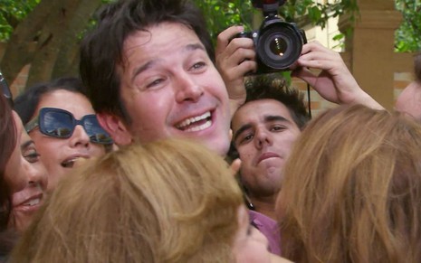 Murilo Benício caracterizado como Ariclenes em cena de Ti Ti Ti: rapaz está rodeado de pessoas e sorri surpreso para alguém fora do quadro