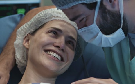 A atriz Leticia Colin está sorrindo e olhando para Humberto Carrão, que usa máscara hospitalar, em cena de parto de Todas as Flores
