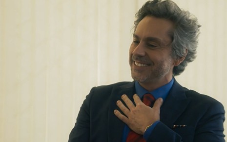 Stenio (Alexandre Nero) sorri com a mão na gravata em cena de Travessia