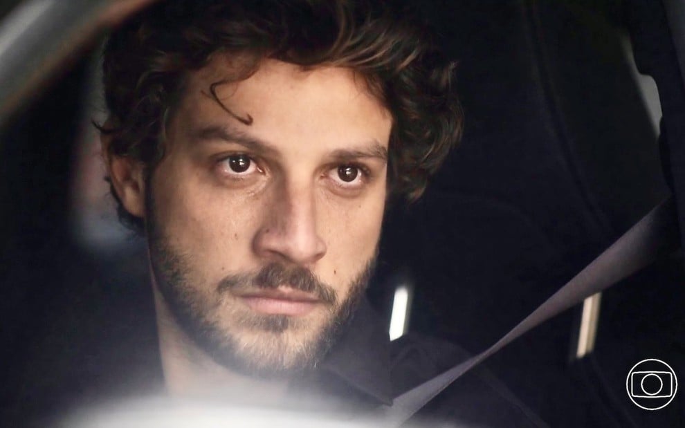 O ator Chay Suede está em um carro e faz uma expressão de raiva em cena da novela Travessia na qual interpreta Ari