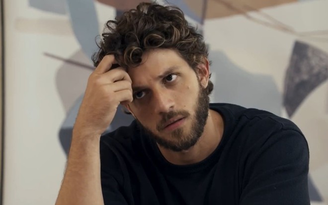Chay Suede caracterizado como Ari; ele usa uma camiseta preta e tem o semblante sério em cena de Travessia