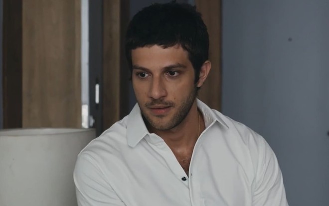 Chay Suede usa camisa branca e está sério em cena da novela Travessia como Ari