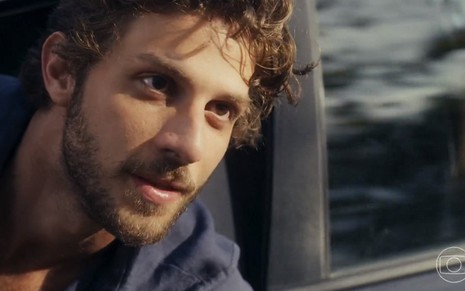 O ator Chay Suede está com camisa azul saindo pela janela de um carro em cena da novela Travessia, da Globo