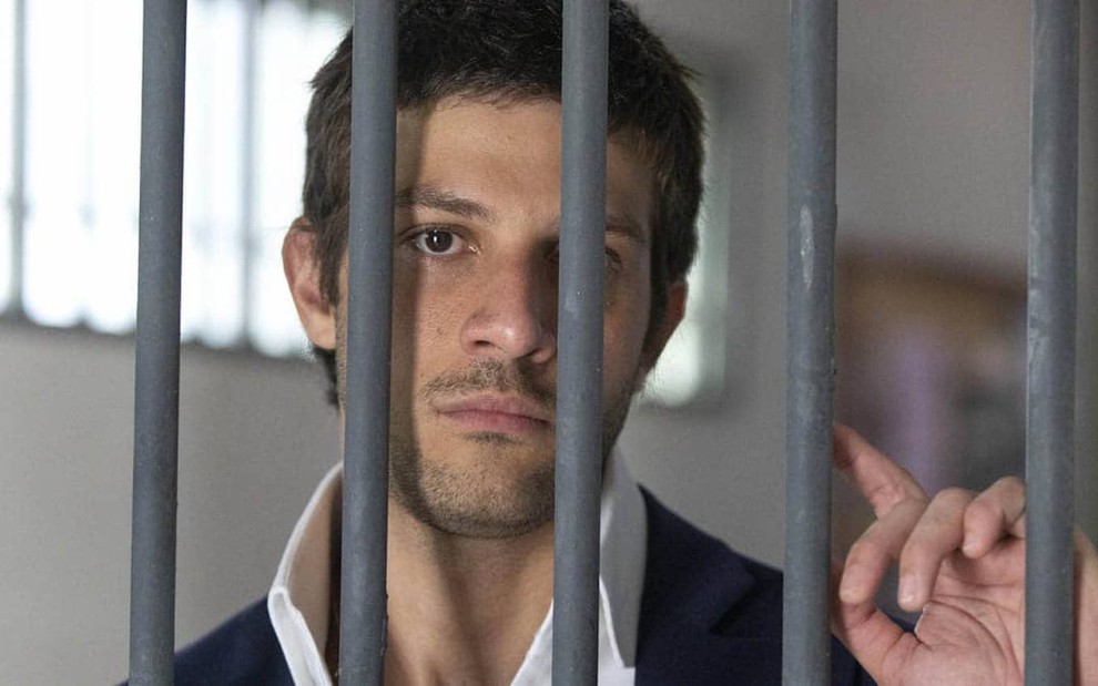 O ator Jay Suede está em uma cela de cadeia em cena de Travessia caracterizado como Ari