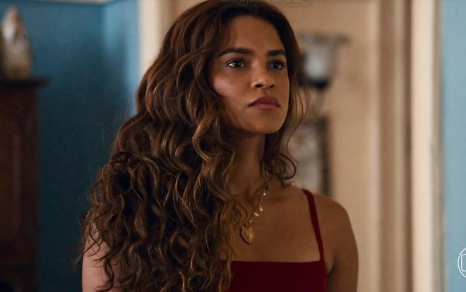 A atriz Lucy Alves em cena da novela Travessia com os cabelos soltos e regatinha vinho