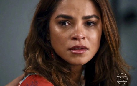 A atriz Lucy Alves está com cabelos soltos e lágrimas nos olhos cem cena de Travessia como Brisa