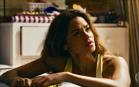 A atriz Lucy Alves olha para o lado em cena de Travessia na qual usa uma regata e está com cabelos soltos como Brisa