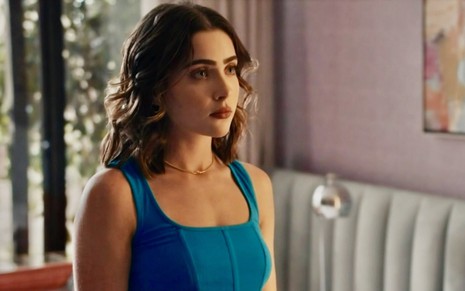 A atriz Jade Picon está com semblante triste em cena da novela Travessia na qual usa regata azul como a personagem Chiara