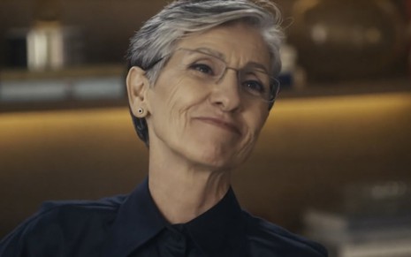 Cassia Kis usa blusa preta e sorri em cena da novela Travessia como Cidália