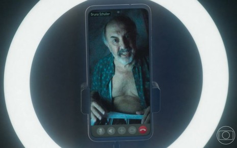 O ator Claudio Tovar aparece em tela de celular com camisa aberta na novela Travessia