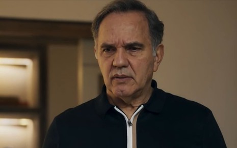 Humberto Martins caracterizado como Guerra em Travessia; ele tem o semblante firme e usa uma camiseta azul em cena da novela