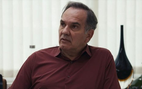 Humberto Martins caracterizado como Guerra em Travessia; ele tem o semblante firme e usa uma camisa vinho de manga comprida em cena da novela