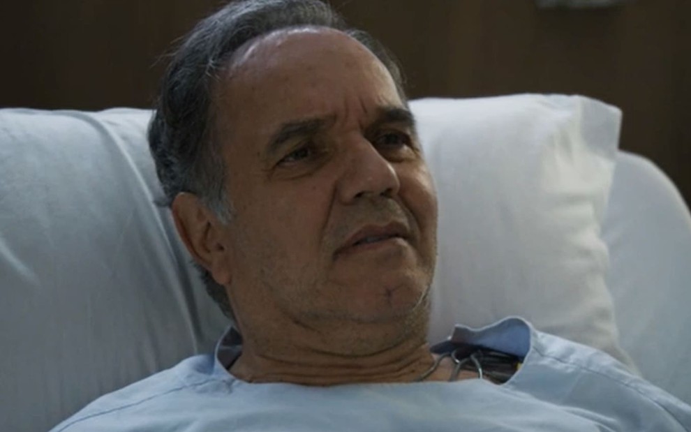 Humberto Martins tem a expressão séria, com o maxilar travado e os olhos fixos, em cena de Travessia; ele está deitado num leito de hospital
