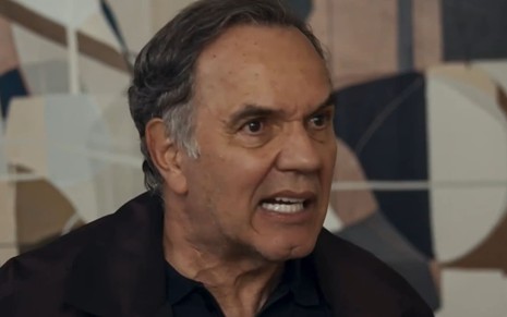 Humberto Martins caracterizado como Guerra em Travessia; ele tem o semblante firme e usa uma camisa preta em cena da novela
