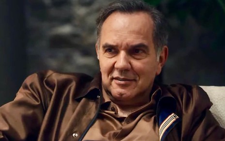 O atro Humberto Martins sorri em cena da novela Travessia na qual usa casaco como o personagem Guerra