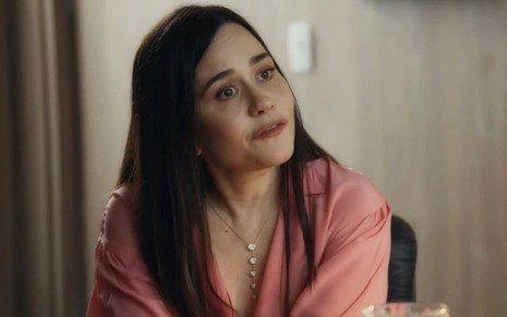 Alessandra Negrini caracterizada como Guida; ela usa uma blusa branca e dá um sorriso vingativo em cena de Travessia