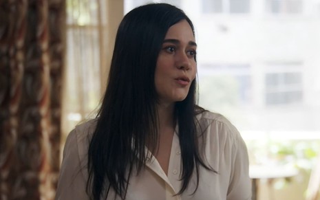 Alessandra Negrini caracterizada como Guida; ela usa uma blusa branca e tem o semblante chocado em cena de Travessia