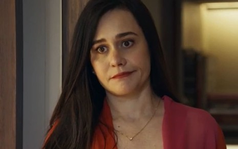 Alessandra Negrini caracterizada como Guida em Travessia; ela tem o semblante abalado e usa uma blusa vermelha em cena da novela