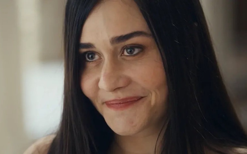 Alessandra Negrini caracterizada como Guida em Travessia; ela dá um sorriso irônico em cena da novela