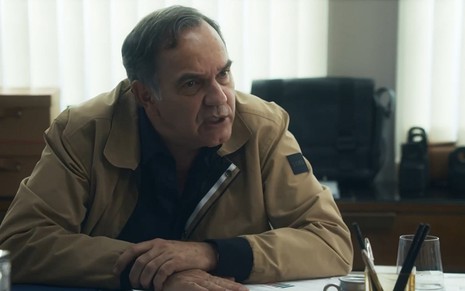Guerra (Humberto Martins) com expressão nervosa sentado atrás de uma mesa de escritório em cena de Travessia