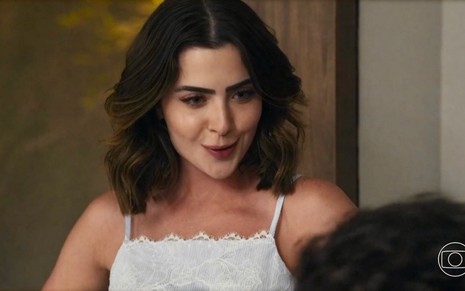 A atriz Jade Picon usa top branco e faz uma expressão de curiosidade em cena de conversa como Chiara em Travessia