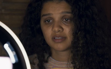 Danielle Olímpia caracterizada como Karina; ela está com lágrimas nos olhos e o semblante abalado em cena de Travessia