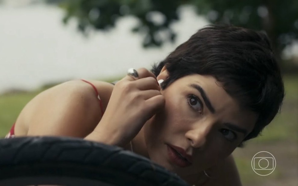 A atriz Vanessa Giácomo está tirando um fone de ouvido e olha com expressão de surpresa para alguém fora da imagem na novela Travessia