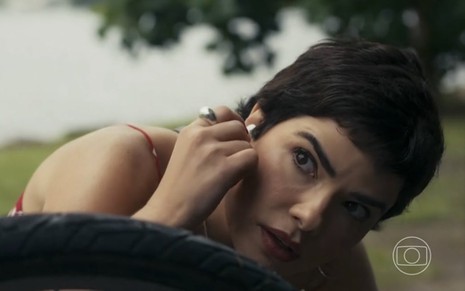 A atriz Vanessa Giácomo está tirando um fone de ouvido e olha com expressão de surpresa para alguém fora da imagem na novela Travessia