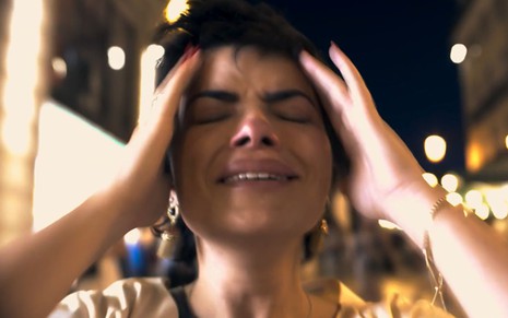A atriz Vanessa Giácomo como Leonor em Travessia; ela está de olhos fechados, chorando, com as duas mãos apoiadas cada uma em um lado da cabeça