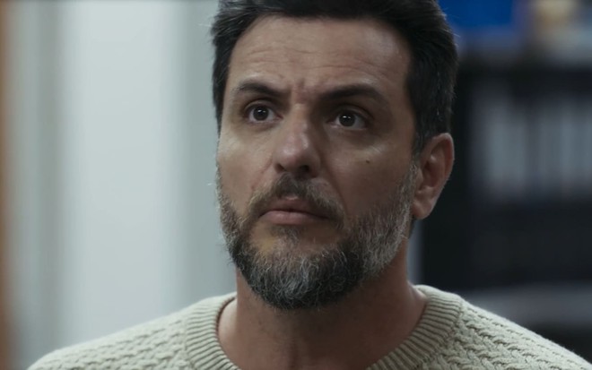 Rodrigo Lombardi caracterizado como Moretti; ator tem as sobrancelhas franzidas e o rosto comprimido em cena de Travessia
