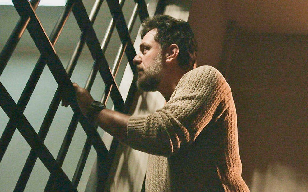 O ator Rodrigo Lombardi está caracterizado como Moretti em cena em uma cela na novela Travessia
