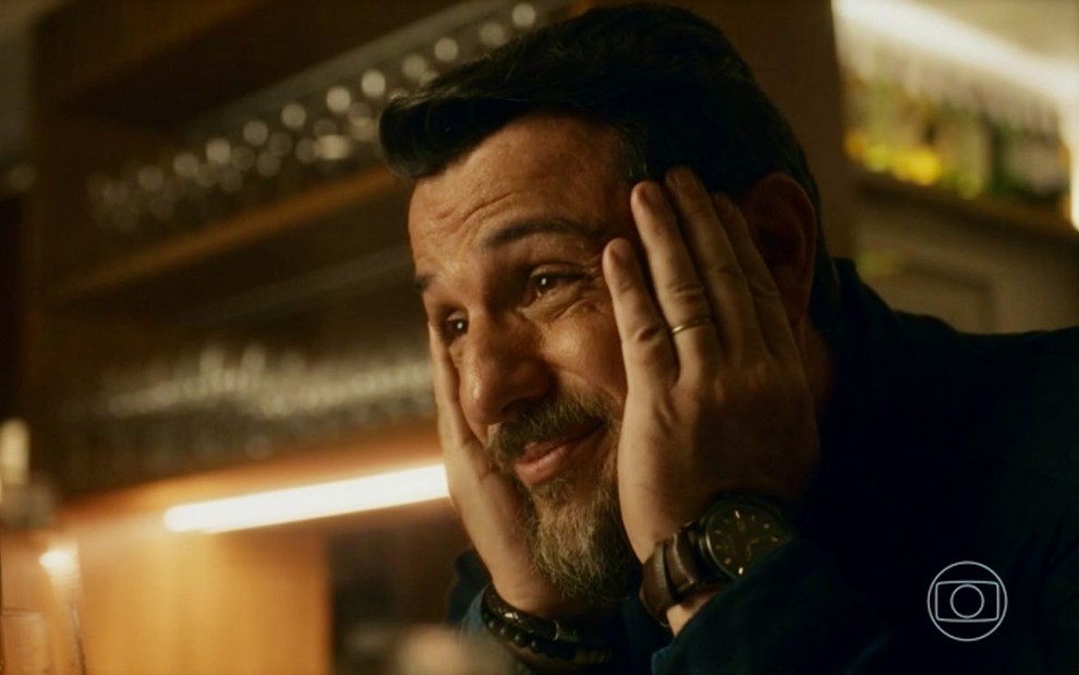 O ator Rodrigo Lombardi está com as mãos no rosto e faz uma expressão de atenção engraçada na novela Travessia, da Globo